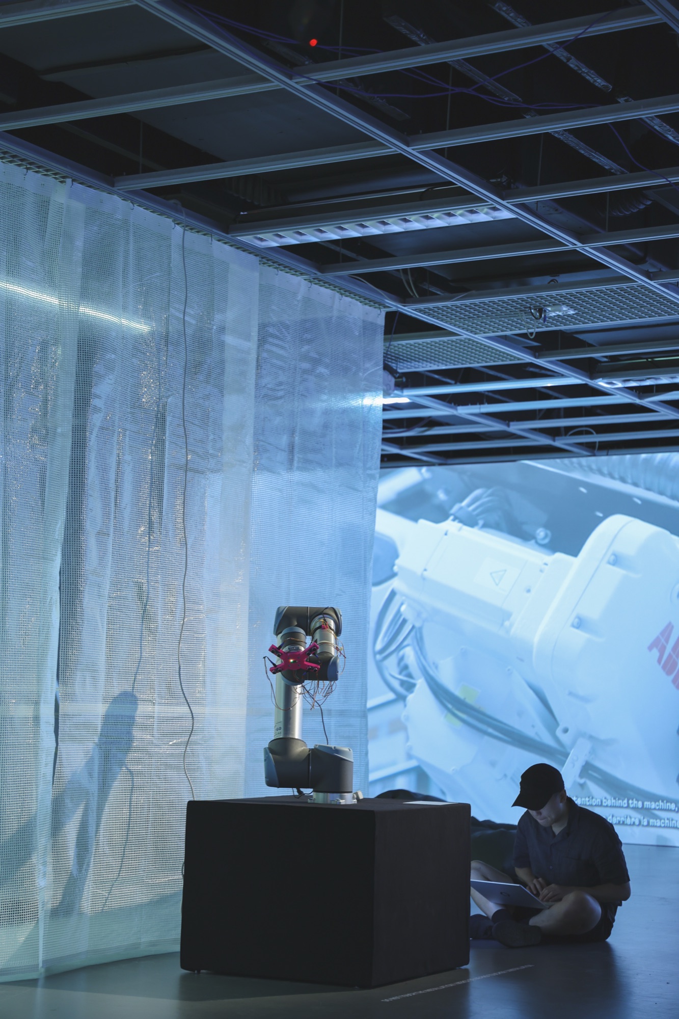 Robot arm on a plinth in the exhibition at Archizoom, with a film projected on the wall behind