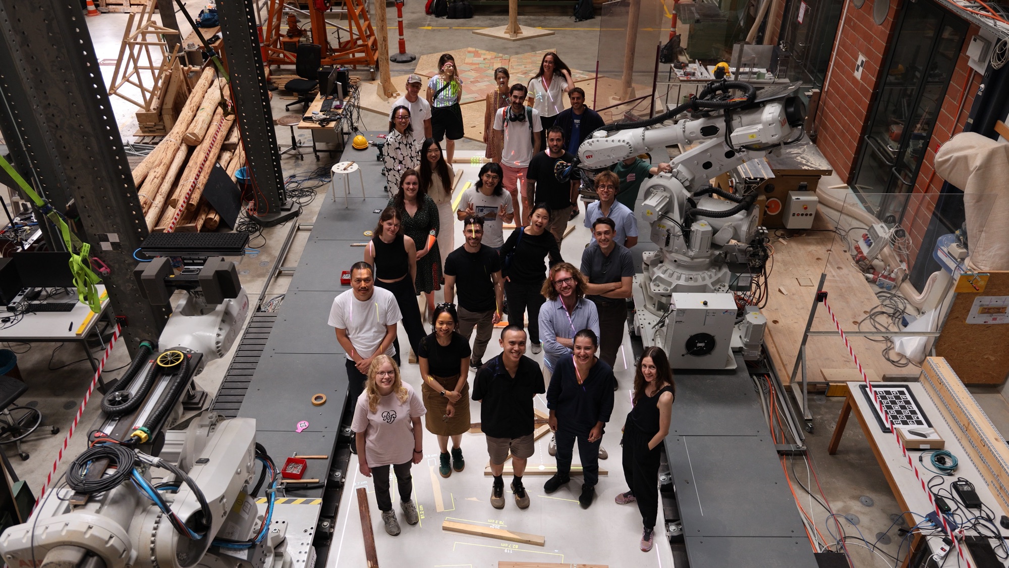 Group photo of the Capitalizing on Uncertainty summer school participants between two industrial robots in the lab